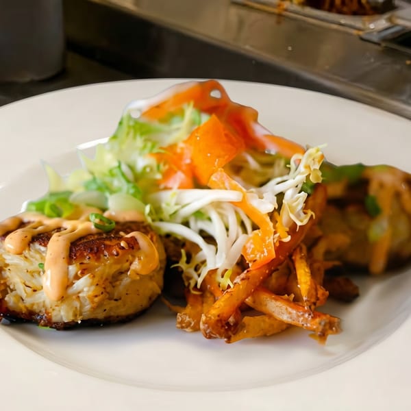 A white plate with a crab cake, fries, and a fresh salad with dressing.