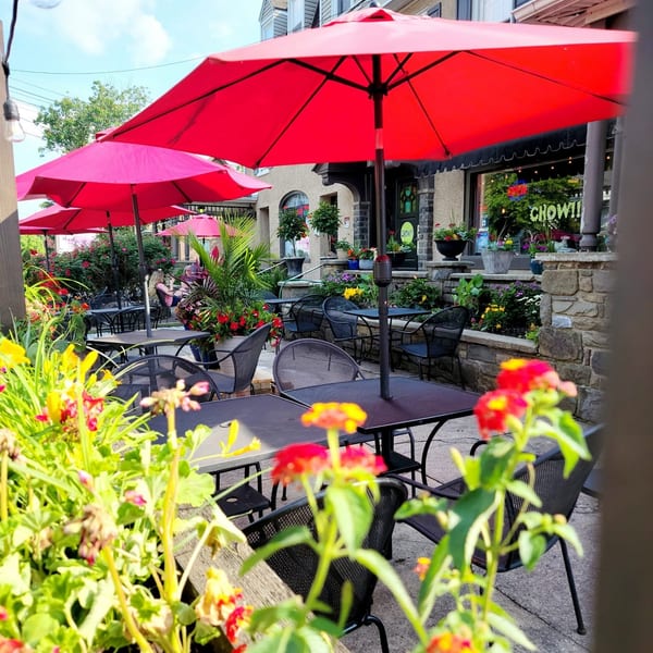Outdoor patio dining area with red umbrellas, black tables and chairs, and vibrant flowers.