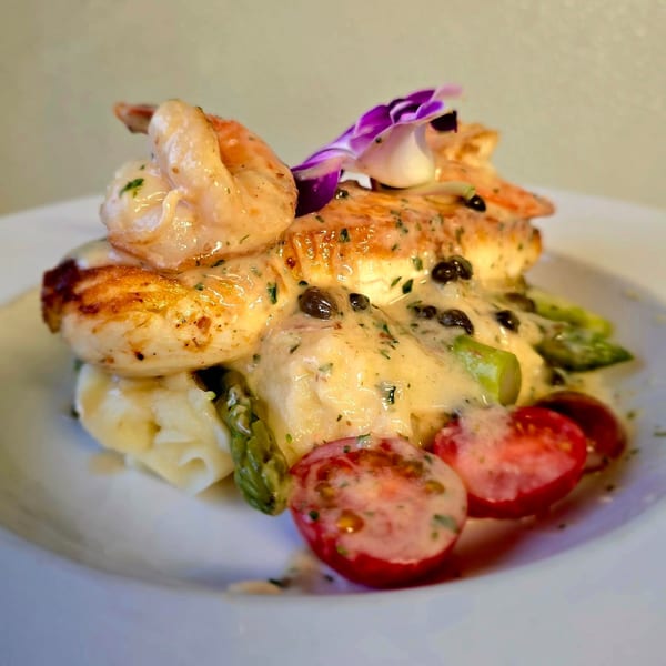 Grilled chicken and shrimp with mashed potatoes, asparagus, cherry tomatoes, and a creamy sauce.