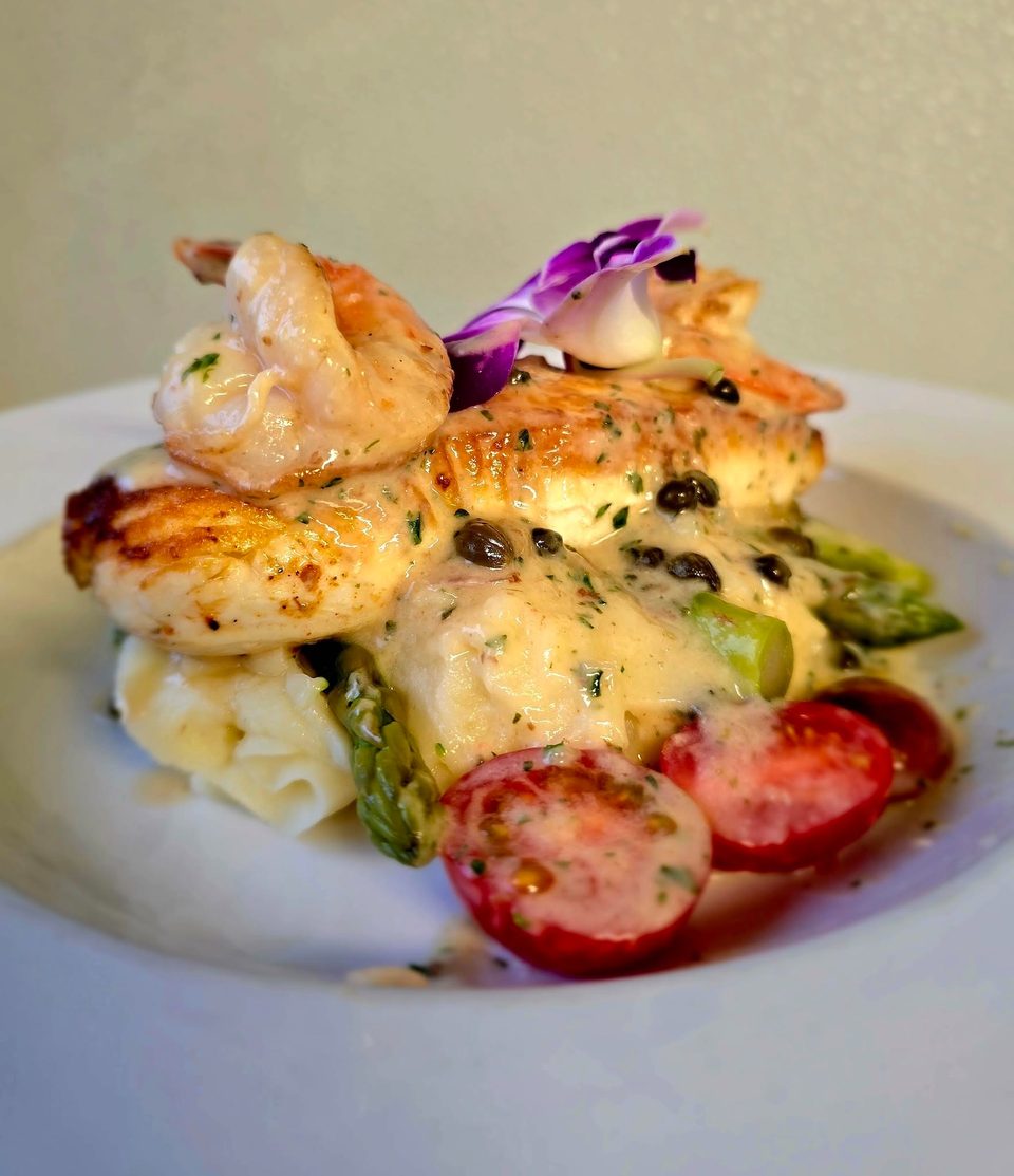Grilled chicken and shrimp with mashed potatoes, asparagus, cherry tomatoes, and a creamy sauce.