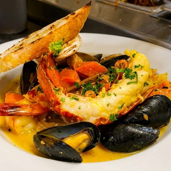 A white bowl filled with seafood stew, including lobster, mussels, shrimp, and toasted bread.
