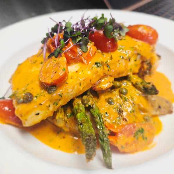 Pan-seared fish with creamy orange sauce, cherry tomatoes, capers, asparagus, and microgreens.