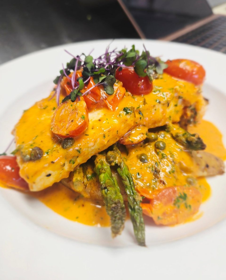 Pan-seared fish with creamy orange sauce, cherry tomatoes, capers, asparagus, and microgreens.