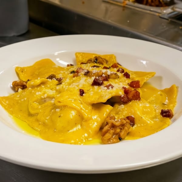 Plate of golden ravioli in a creamy sauce, topped with walnuts, bacon bits, and grated cheese.