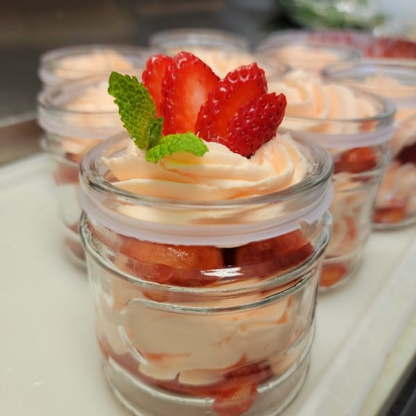 Strawberry shortcake parfaits in small glass jars, topped with whipped cream and mint.