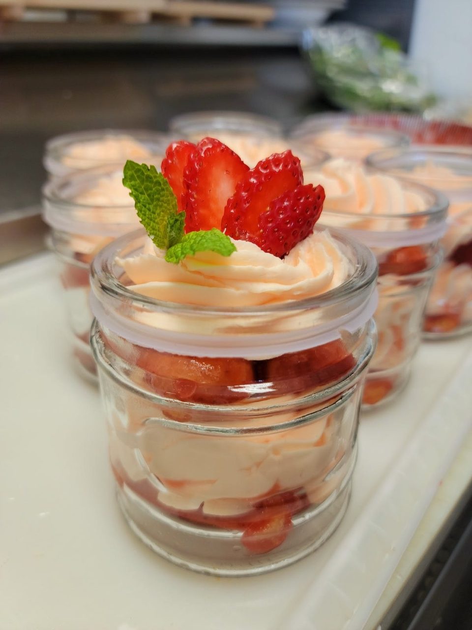 Strawberry shortcake parfaits in small glass jars, topped with whipped cream and mint.
