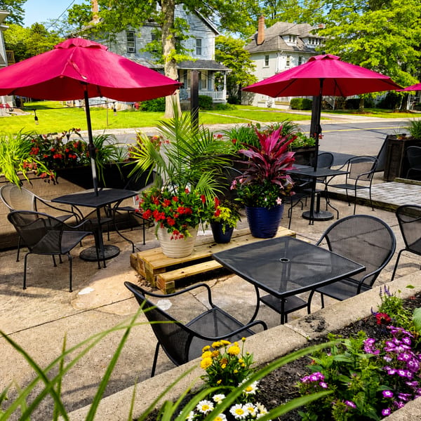 Outdoor patio with black metal tables and chairs, vibrant pink umbrellas, and colorful potted plants.