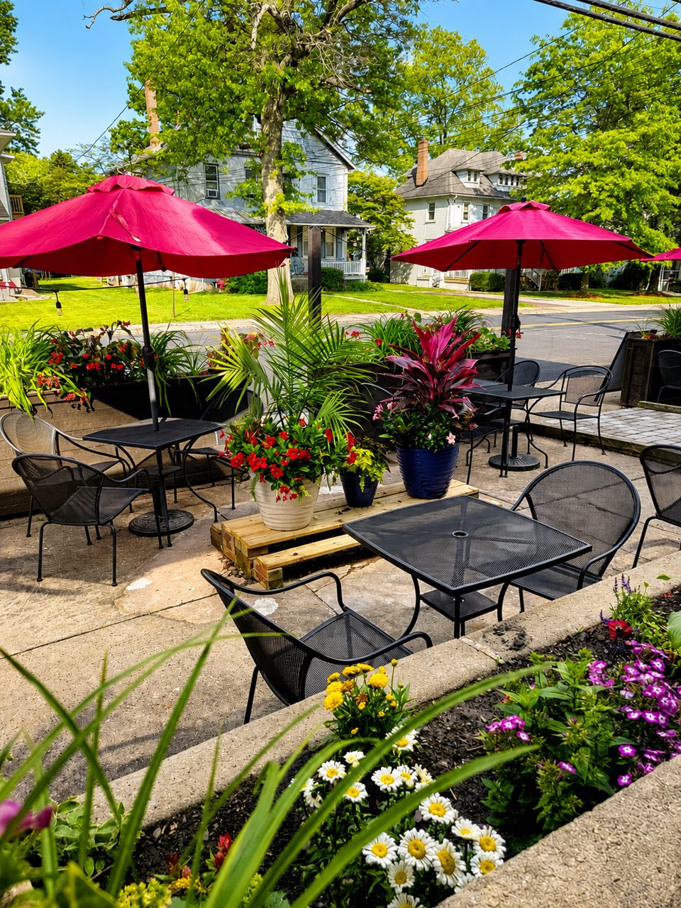 Outdoor patio with black metal tables and chairs, vibrant pink umbrellas, and colorful potted plants.