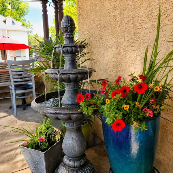 Tiered fountain and vibrant red and yellow flowers in planters on a restaurant patio.