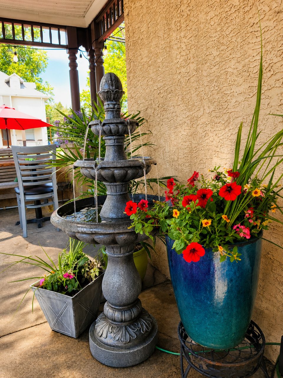 Tiered fountain and vibrant red and yellow flowers in planters on a restaurant patio.